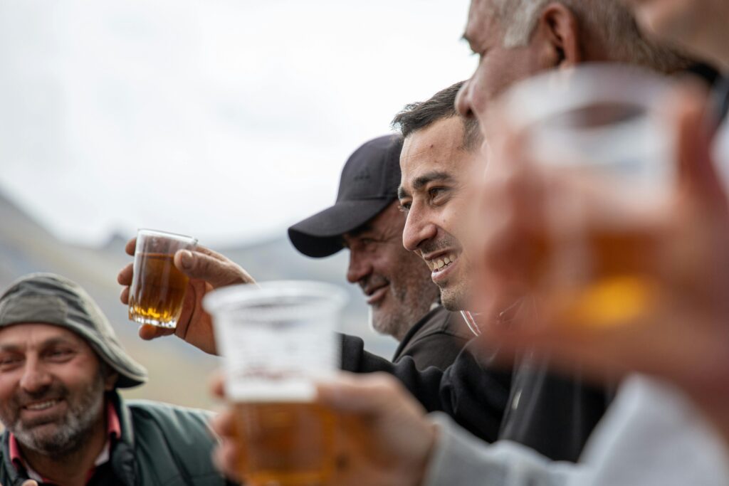 Joyful group of men raising beer glasses in a toast, captured in the scenic outdoors of Imereti, Georgia.