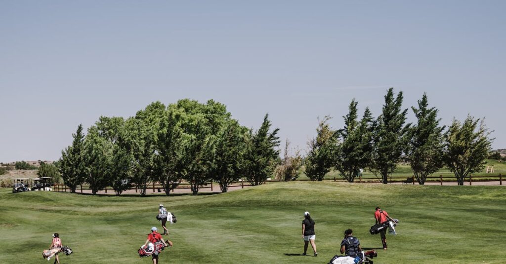 Golfers carrying bags on a lush green course under a clear blue sky.