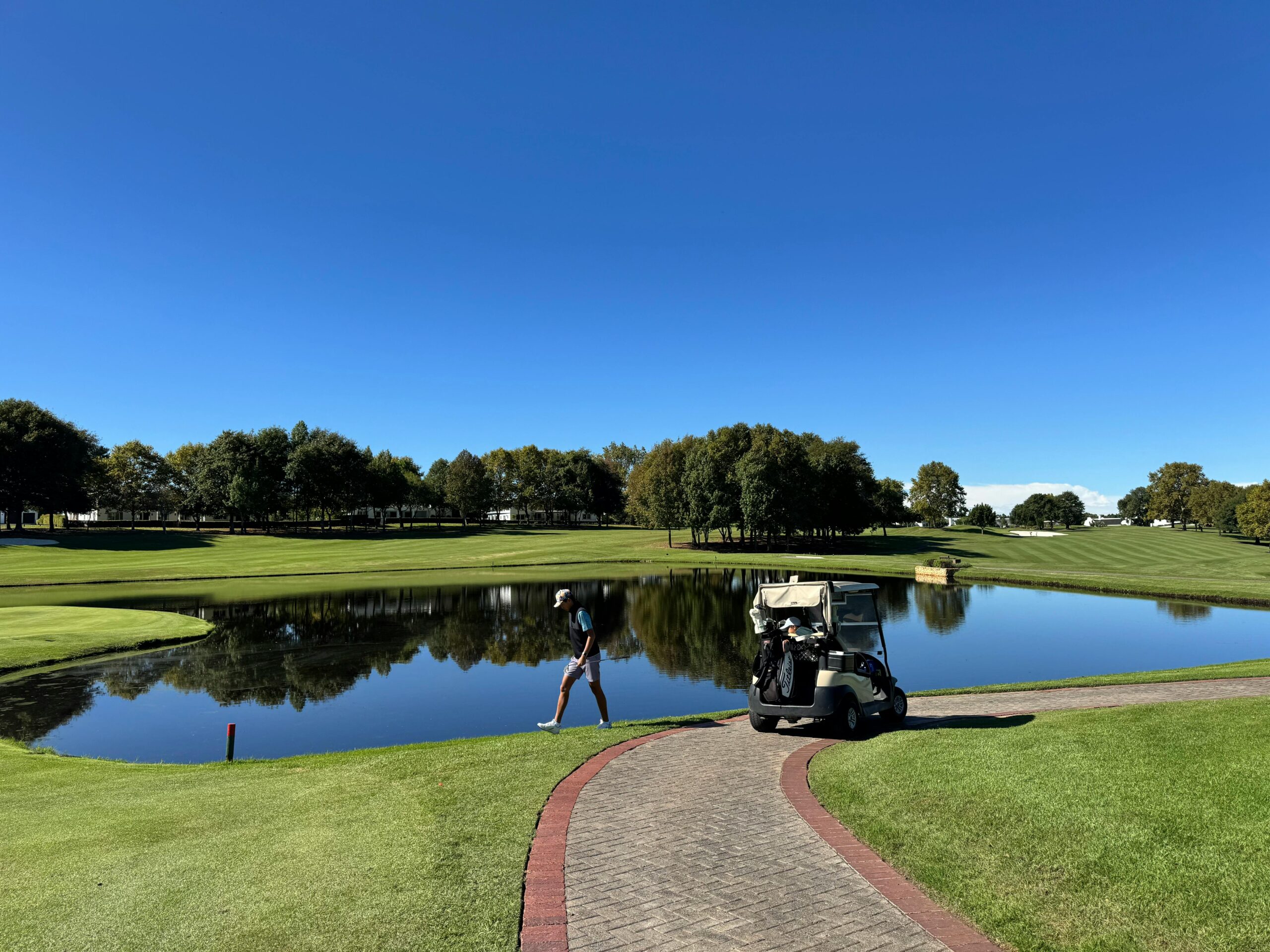 A golfer with a cart by a peaceful pond on a sunny day, ideal for outdoor leisure.